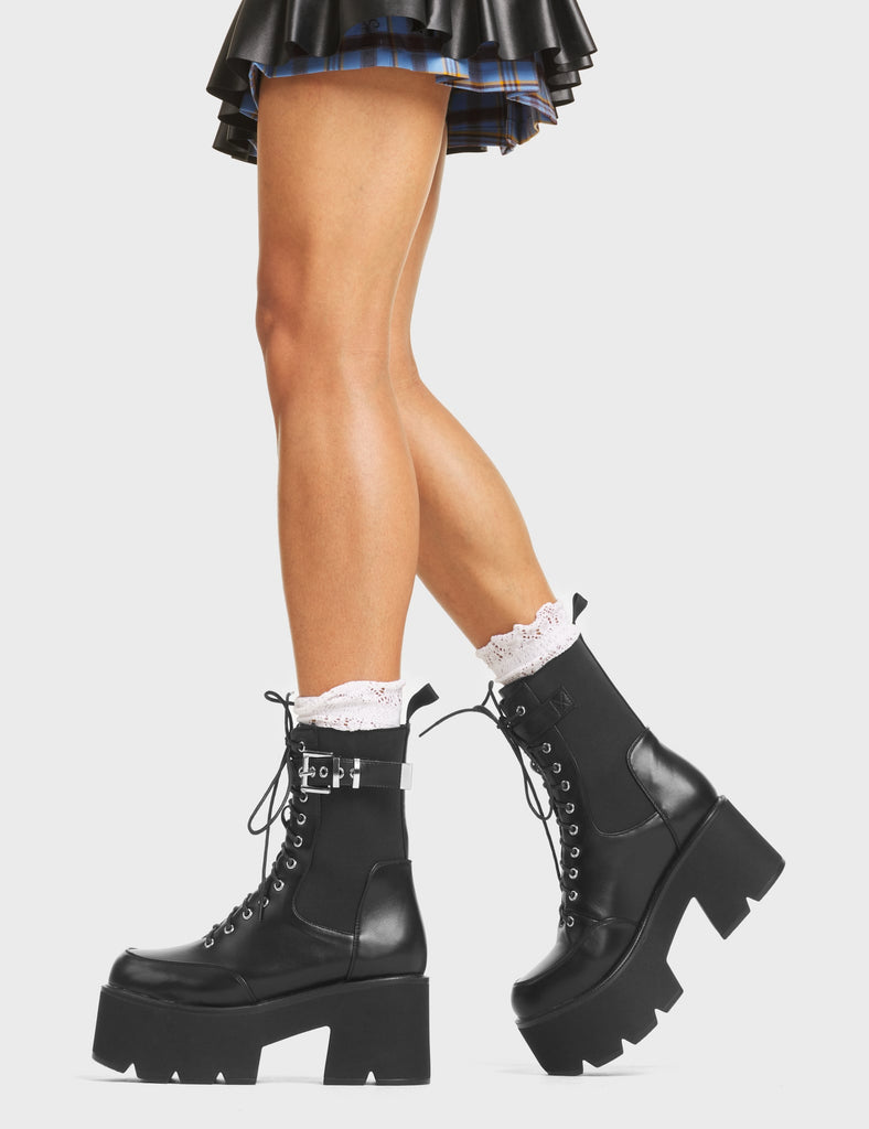 Rocket Chunky Platform Ankle Boots in Black faux leather. These platform boots feature a lace-up design and a thick strap with faux leather around the ankle featuring a silver square-shaped buckle. They also have a black stretchy gusset and a pull-on tab for an easy fit. Made with eco-friendly materials and 100% cruelty-free!